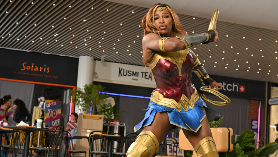 serena williams dressed as wonder woman playing tennis in a retro shopping mall